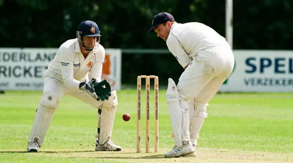 Cricketspeler springt naar de bal terwijl wicket-keeper alert wacht achter de stumps